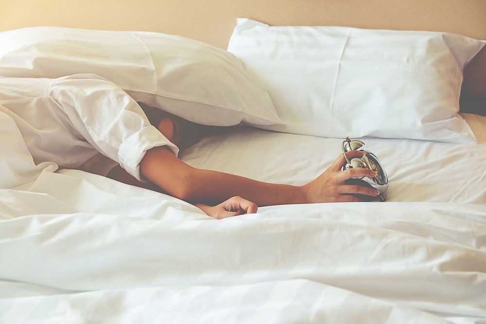 Irritated young woman putting her alarm clock off in the morning with soft morning light.
