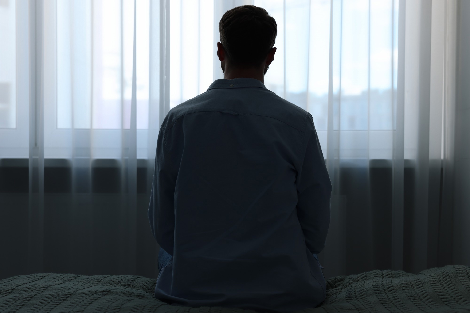 ad man sitting on bed at home, back view.