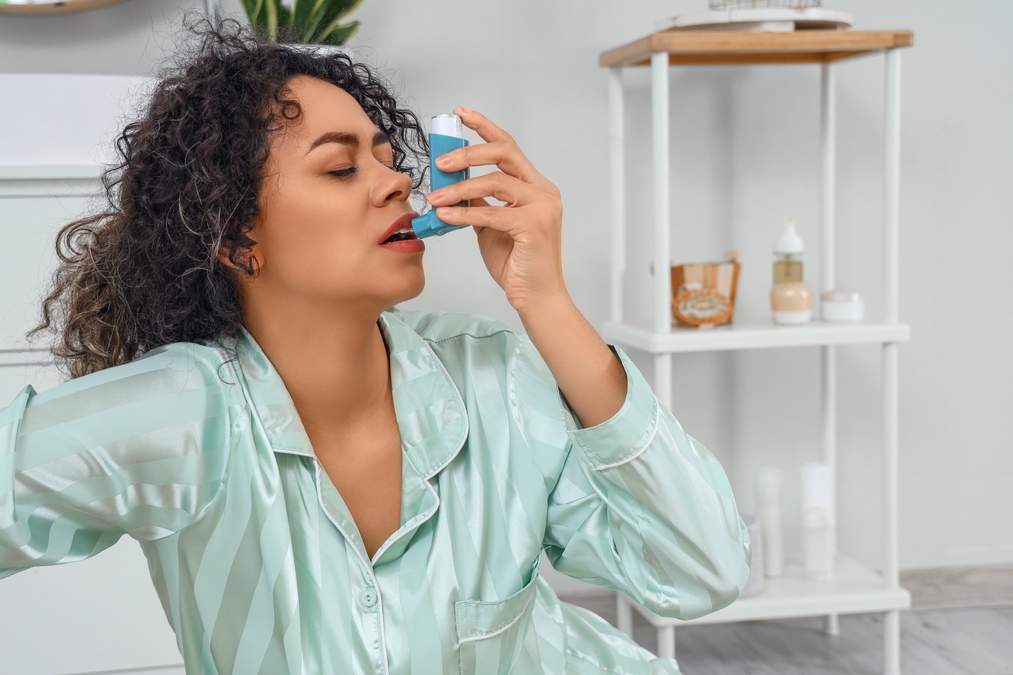 Young African-American woman using asthma inhaler in bathroom.
